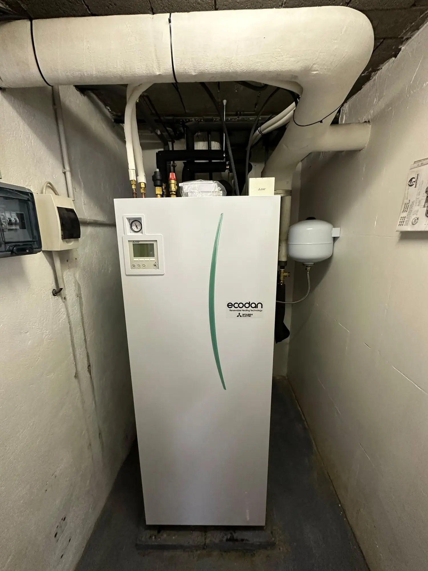 Local technique en sous-sol avec gaines calorifugées fixées au plafond et module intérieur de pompe à chaleur contre le mur.